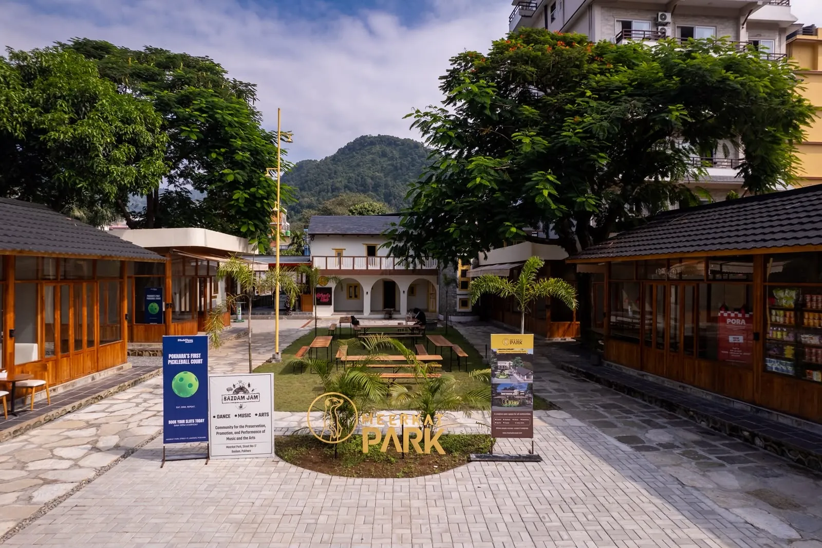 Meerkat Park on Lakeside: wooden stalls around a lawn with benches, under big trees and green hills